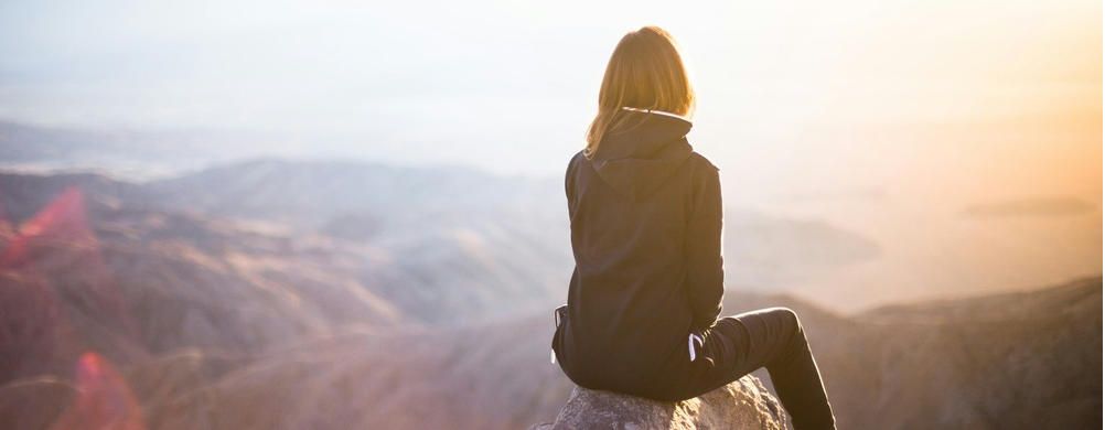 young girl sits on the ledge of a cliff looking off into the distance