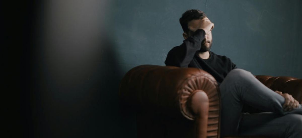 man sits on a leather couch with his head in his hands as he struggles with mental health