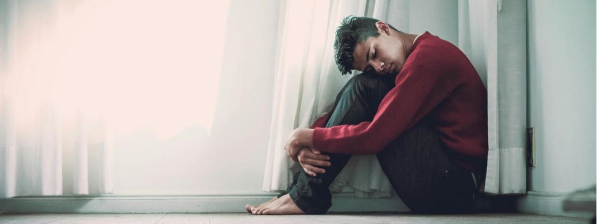 young man is sitting on the floor with his head in his knees struggling with mental health issues