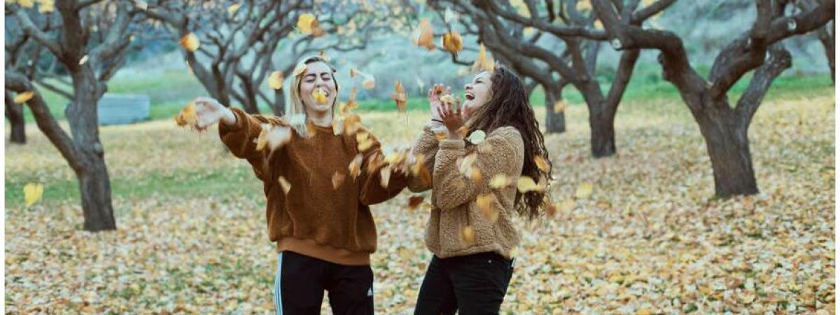 two girls happily throwing falling leaves up in the air