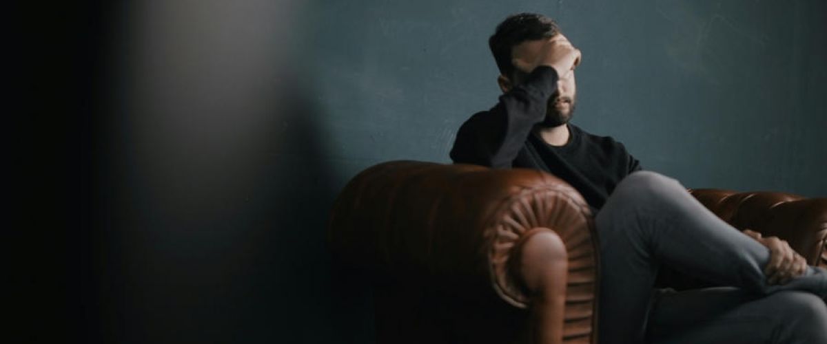 man sits on a leather couch with his head in his hands as he struggles with mental health