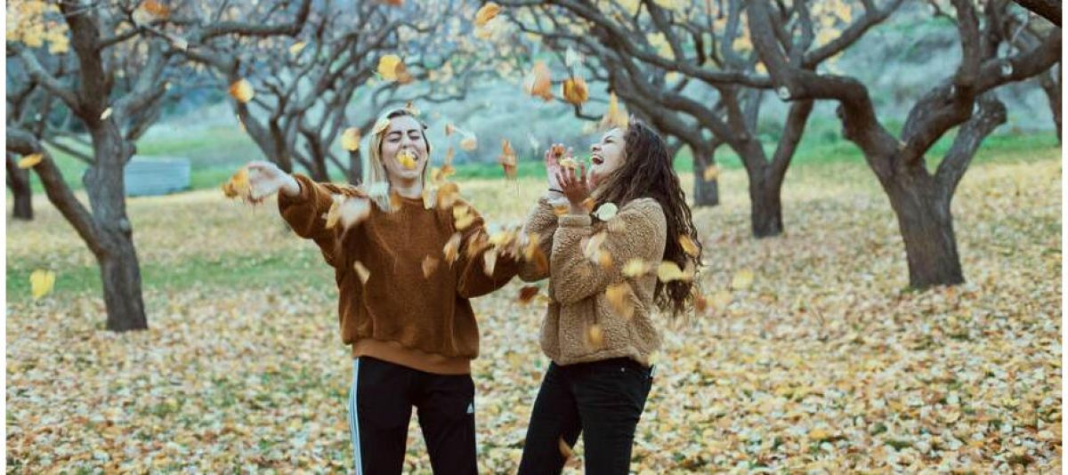 two girls happily throwing falling leaves up in the air