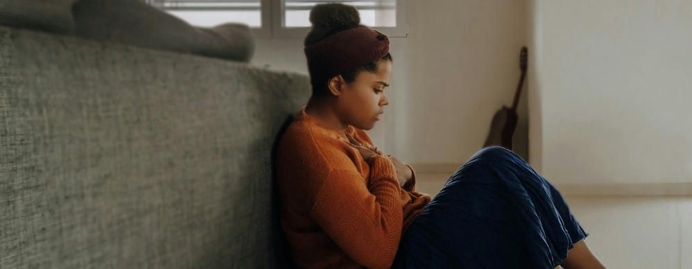 young girl sits on the floor holding her chest as she struggles with mental health