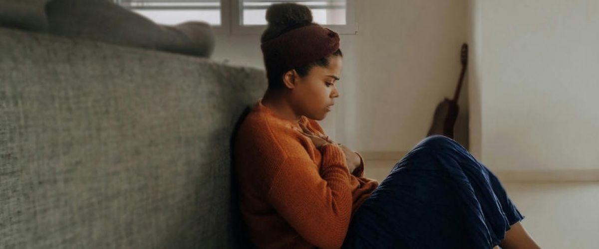 young girl sits on the floor holding her chest as she struggles with mental health