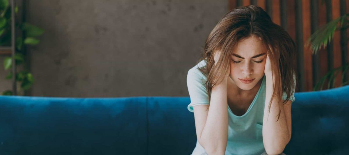 a women sits on a blue couch with her head in her hands struggling with addiction