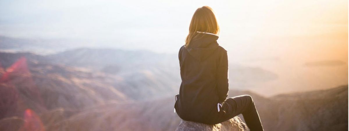 young girl sits on the ledge of a cliff looking off into the distance