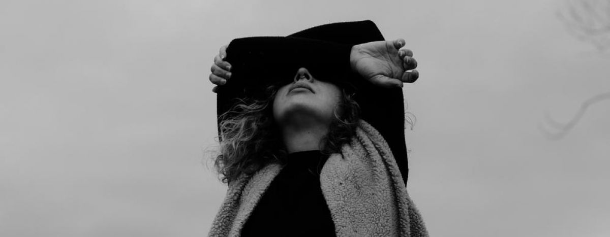 young girl with curly hair wraps her arms around her face as she looks up